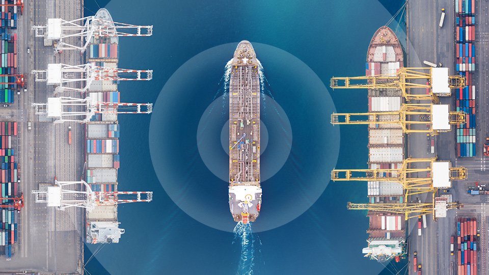 Aerial view of oil tanker moving between two container docks with container ships and cranes. Concentrics rings superimposed over the oil tanker representing radar as if the ship was autonomous