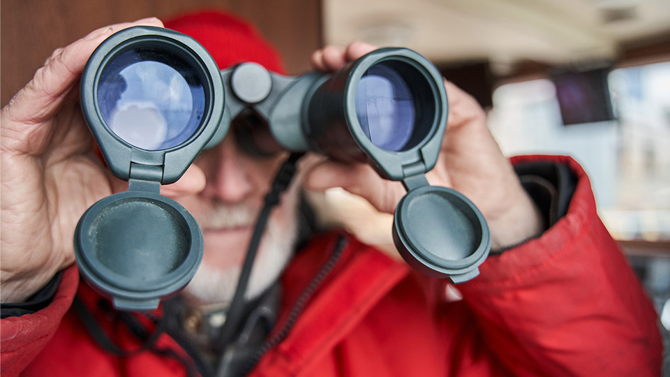 Man in red coat looking through binoculars