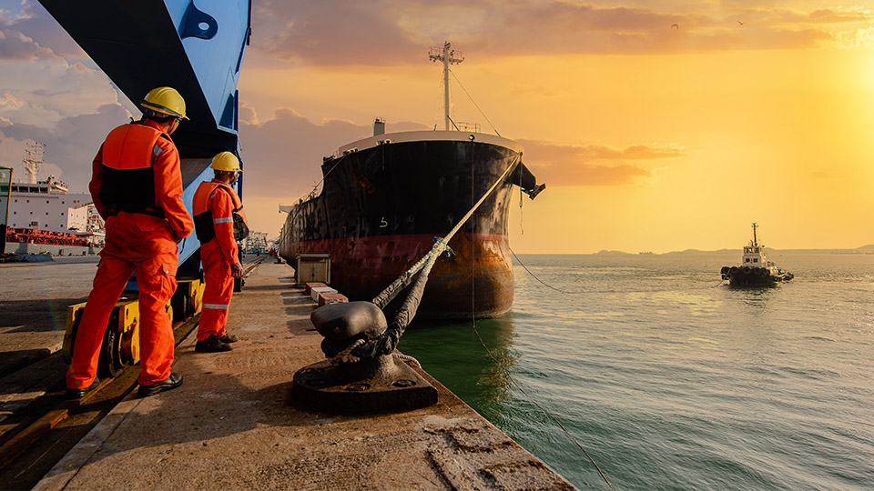 Mooring men standing near a docked ship and tug at sunset/sunrise
