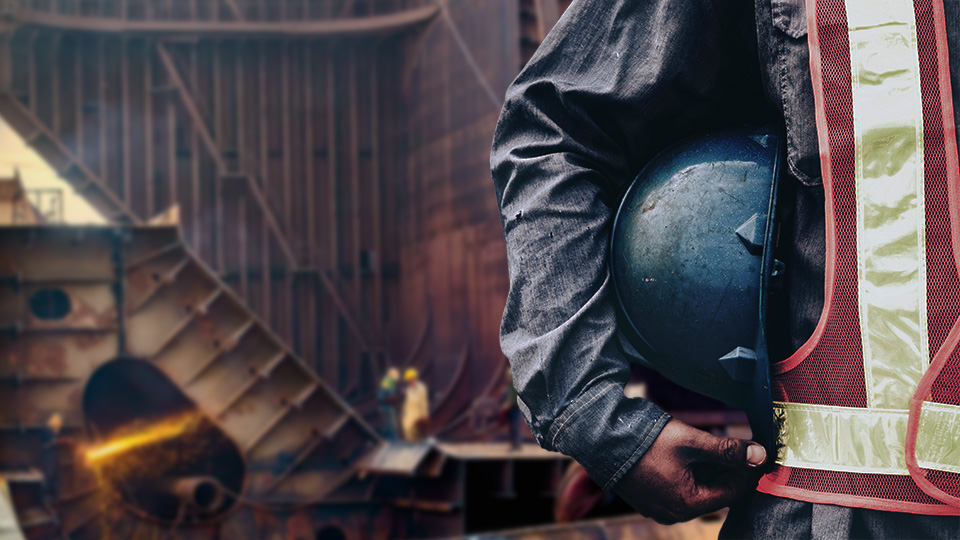 Close-up of worker arm holding hard hat; background blurred image of workers recycling ship