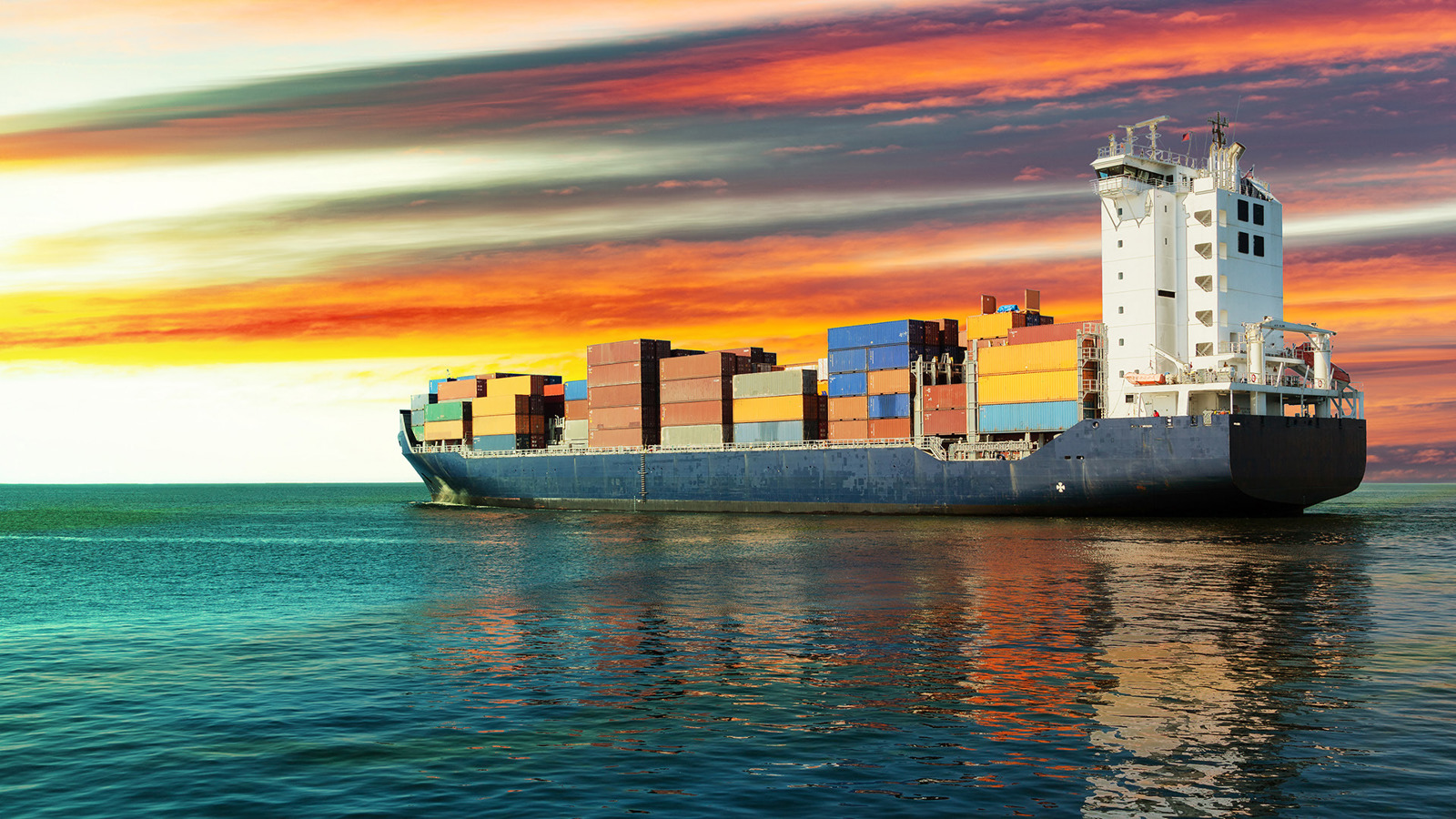 Container ship on the sea with a vibrant sunrise/sunset on the horizon