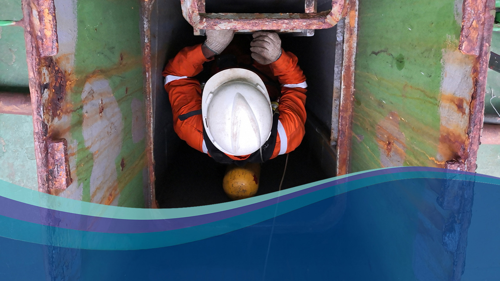 seafarer wearing white safety hat climbing down a ship's hatch
