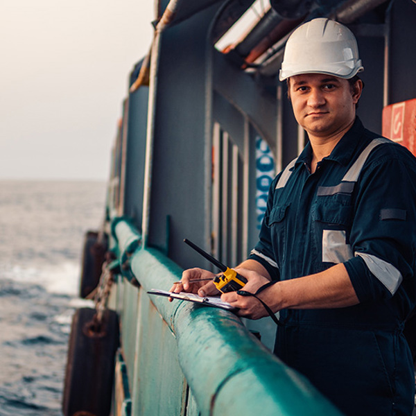 Deck officer standing at a ship's railing with a clipboard and walkie talkie.