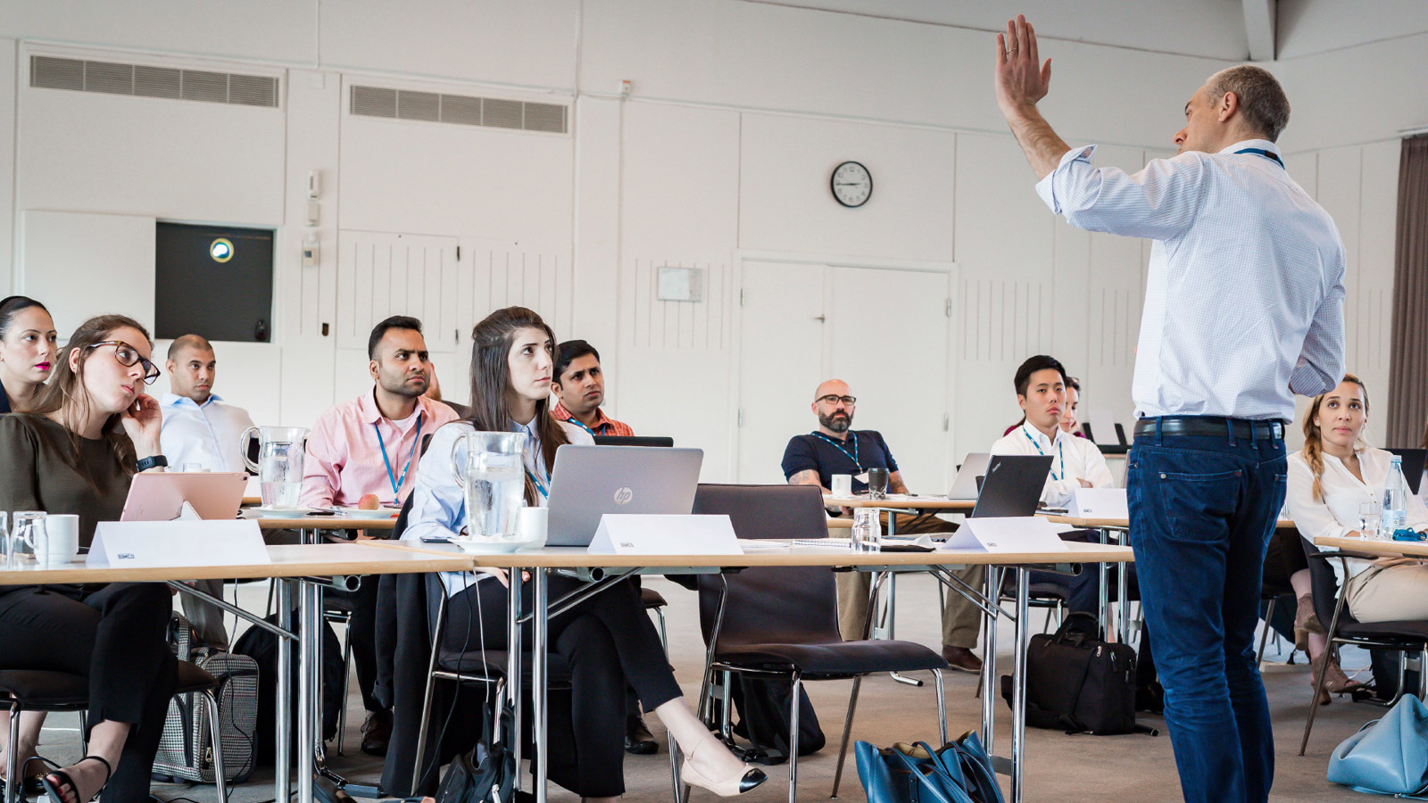 Man standing at the front of a classroom setting with course attendees watching him intently
