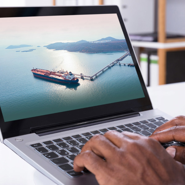 Laptop screen showing a tank ship at a terminal, with hands on keyboard