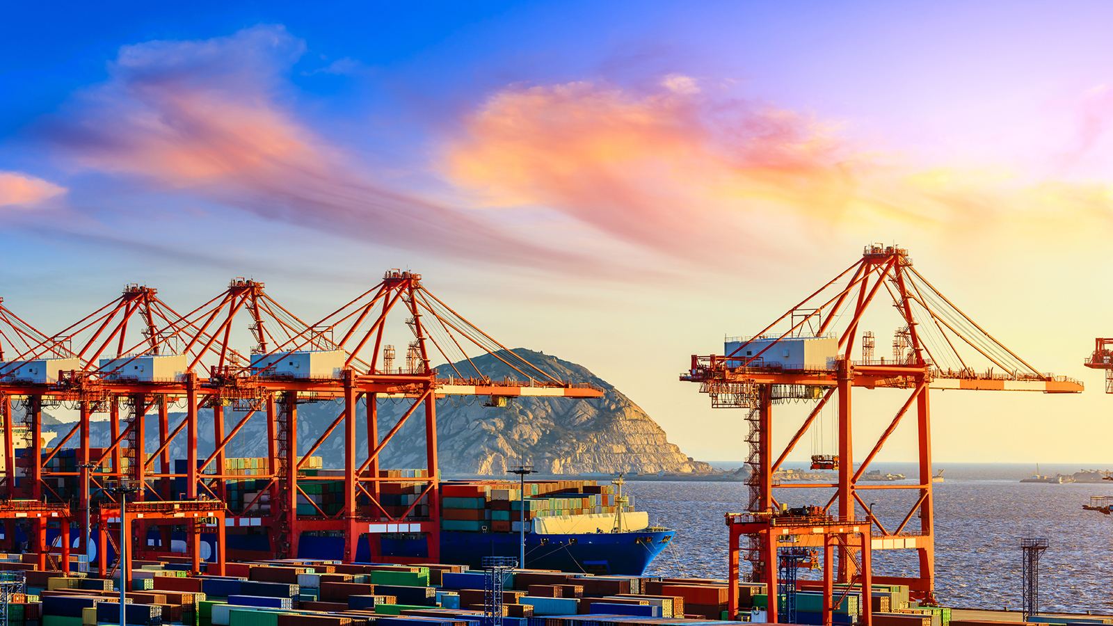 Container cranes over a container ship moored at berth with sunset in background